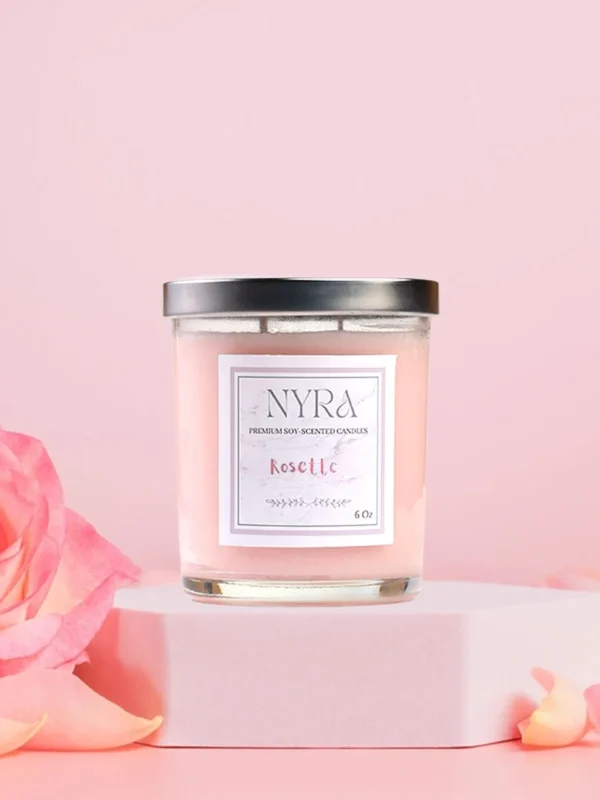 a pink candle on a pink surface next to a pink rose