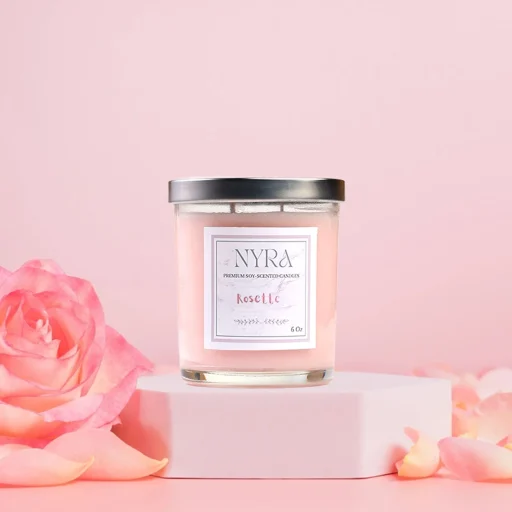 a pink candle on a pink surface next to a pink rose